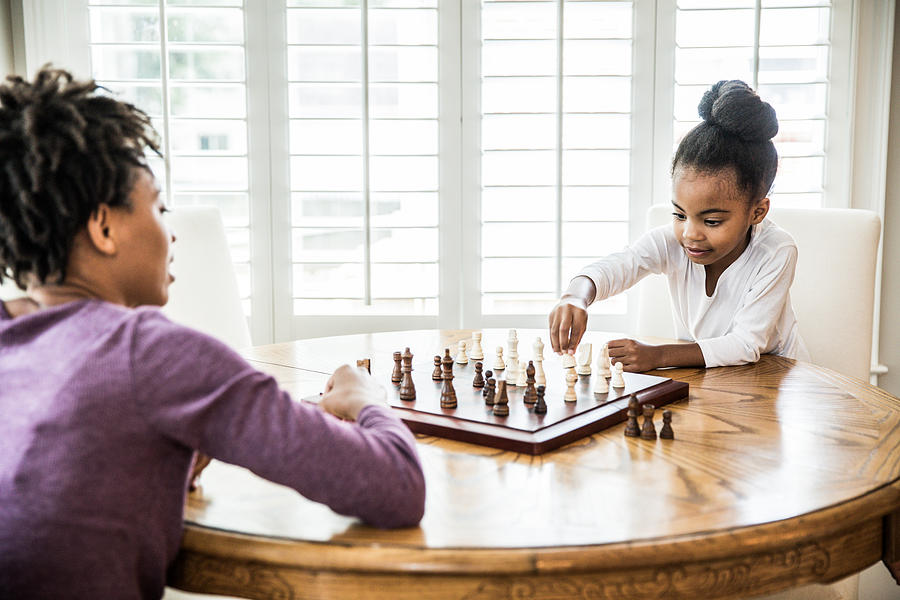 Young girl (6yrs) playing chess with mother Photograph by MoMo Productions