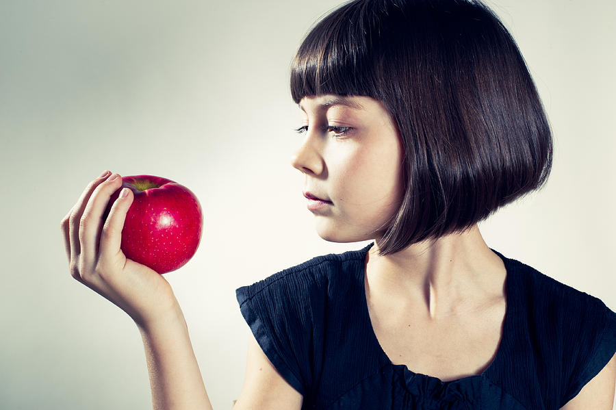 Young girl about to eat a red apple. Photograph by Martinedoucet