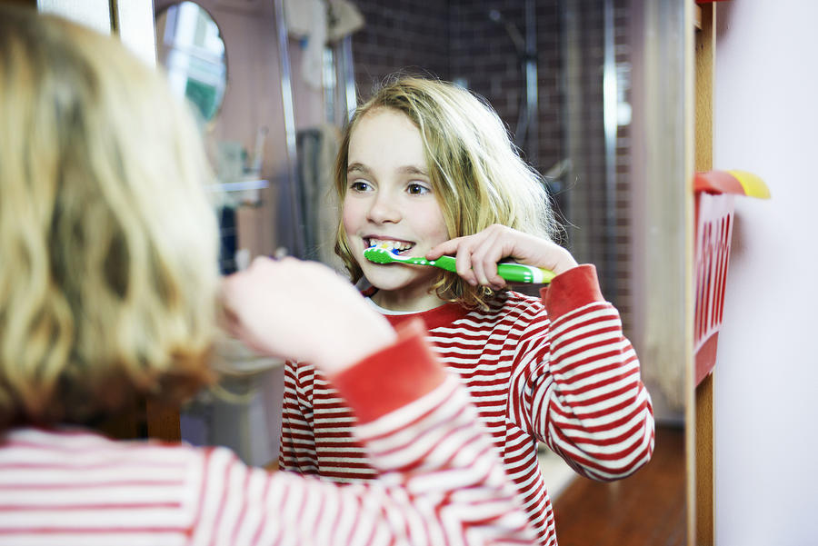Young Girl Brushing Teeth In Bathroom Mirror Photograph by Tara Moore