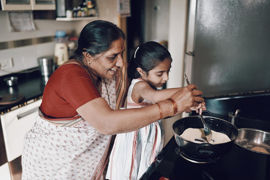 Young girl helping her grandmother while working in the kitchen Photograph by Mayur Kakade