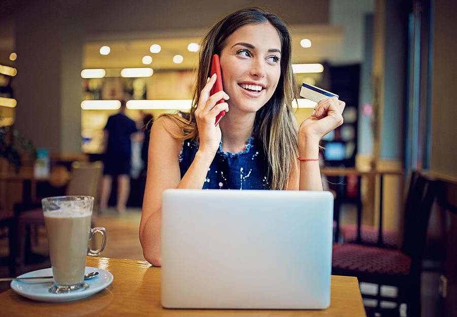 Young girl is sitting in a cafe, and shopping online using her credit card Photograph by Praetorianphoto