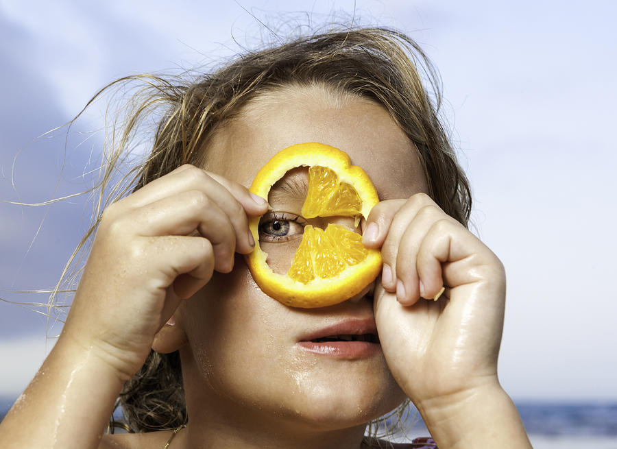 Young girl looking through slice of orange Photograph by Marcos Welsh