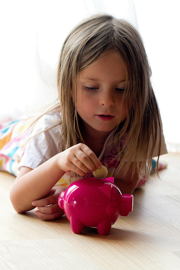 Young girl putting coin in piggy bank Photograph by Lacaosa