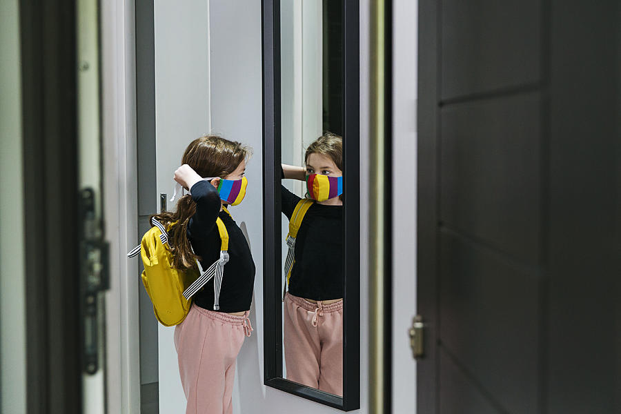 Young girl putting on her face mask in mirror by front door Photograph by Justin Paget
