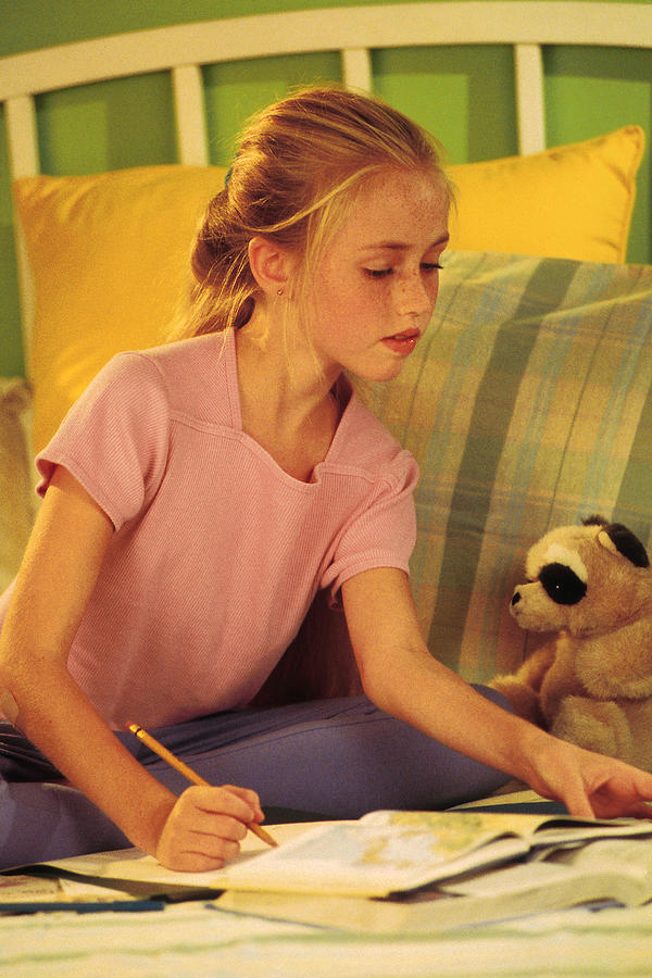 Young girl sitting on bed doing homework Photograph by Comstock