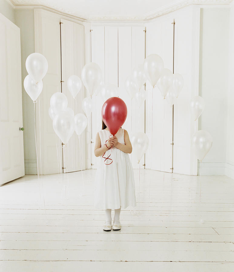 Young Girl Standing Behind a Red Balloon in a White Room Photograph by Lottie Davies