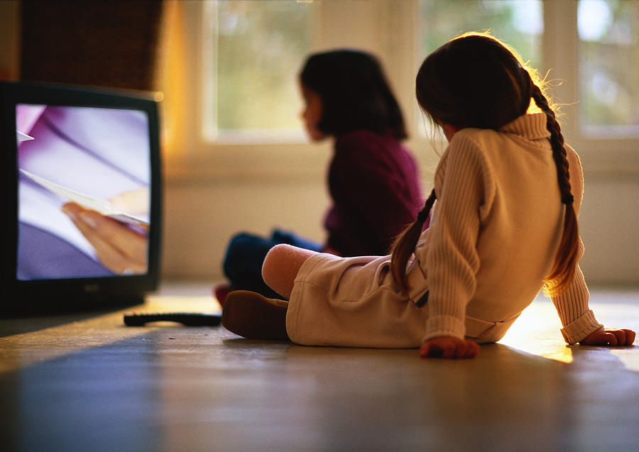 Young girls sitting on wood floor watching TV, girl in background blurred. Photograph by Gerard Launet