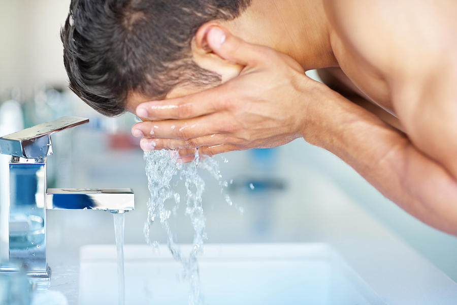 Young guy cleansing face with water at the sink Photograph by Goodboy Picture Company