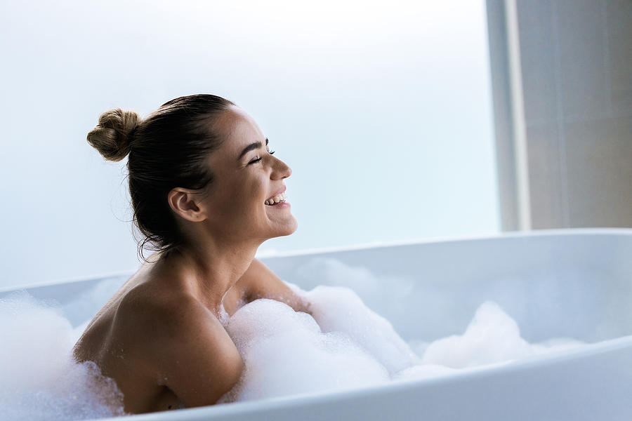 Young happy woman enjoying in bubble bath with her eyes closed. Photograph by Skynesher