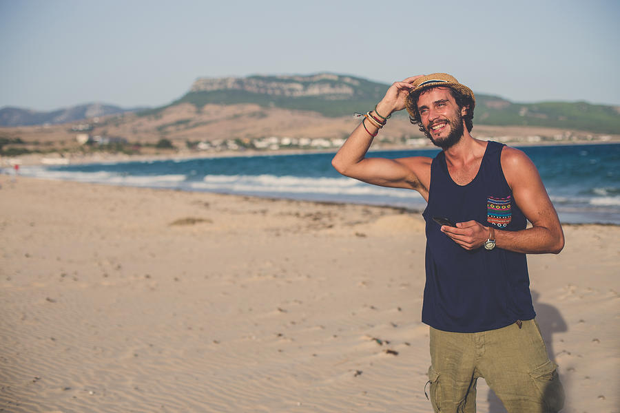 Young Hipster man at the beach using phone Photograph by South_agency
