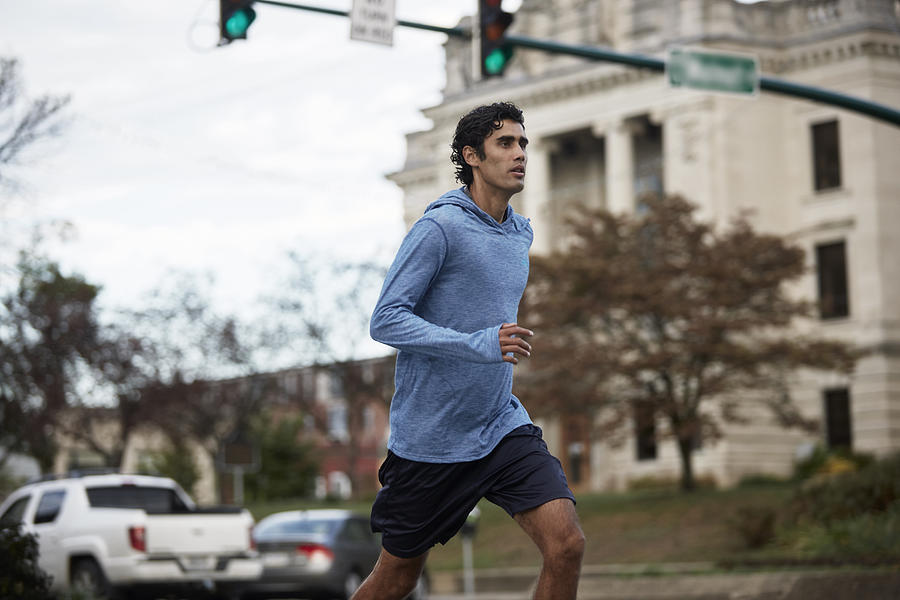 Young Latino man in blue sweatshirt runs by small town courthouse Photograph by Patrick Fraser