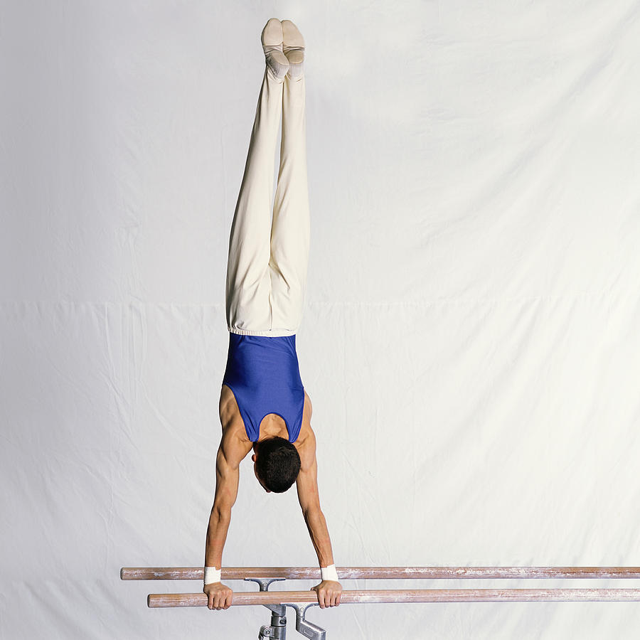Young male gymnast performing routine on parallel bars, rear view. Photograph by Dominique Douieb