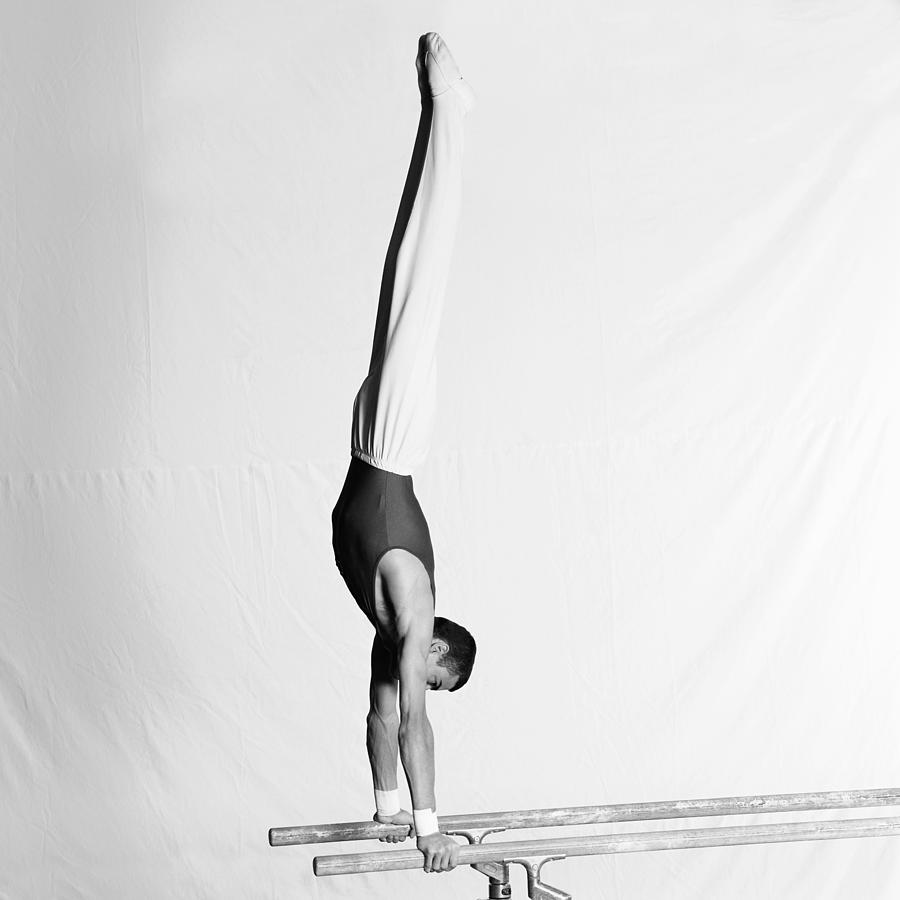 Young male gymnast upside down on parallel bars, side view. Photograph by Dominique Douieb