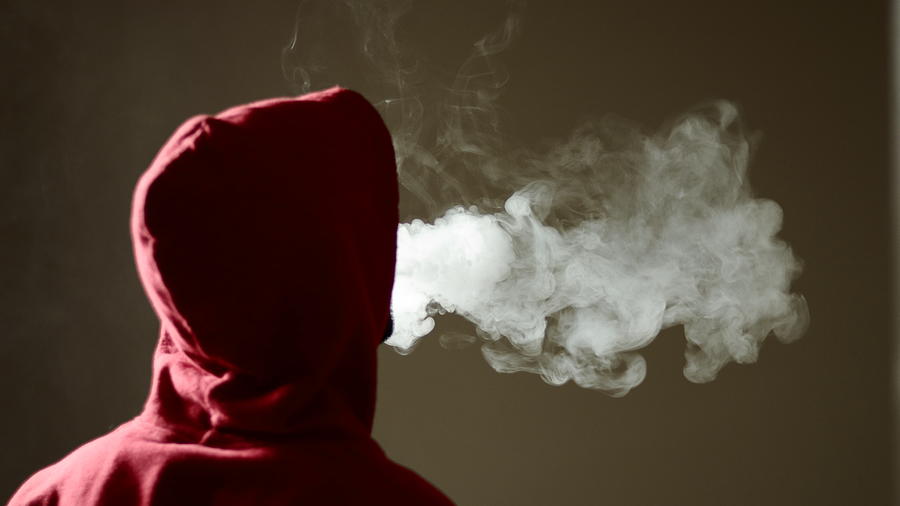 Young male in red hoodie vaping smoking, exhales thick vapor, isolated rear view Photograph by property of Naveen Asaithambi