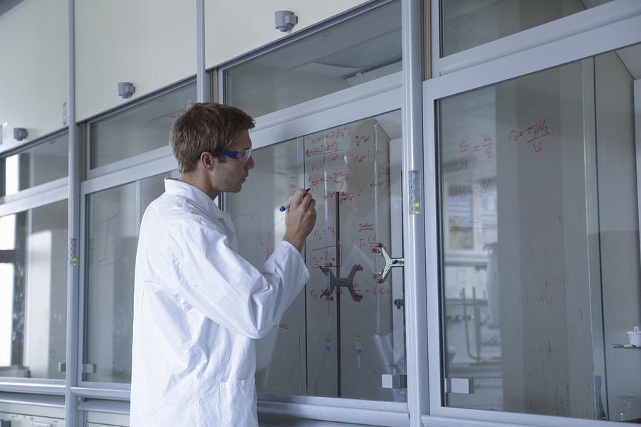Young male scientist writing results on fume cupboard window Photograph by Sigrid Gombert