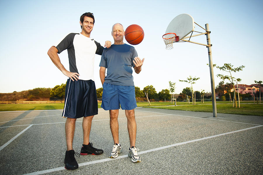 Young man and senior man on outdoor basketball court, portrait Photograph by Peter Griffith
