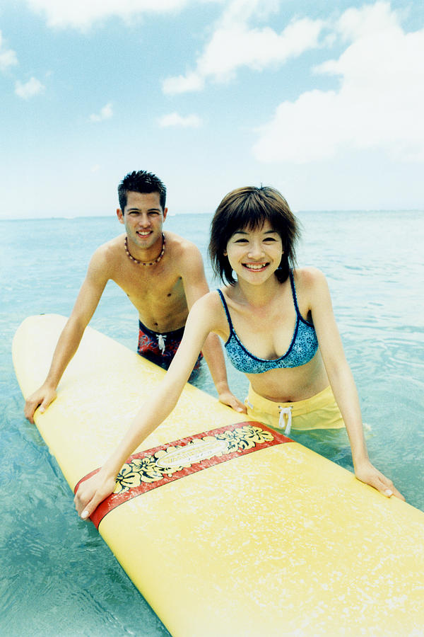 Young man and woman holding surfboard in water Photograph by Dex Image