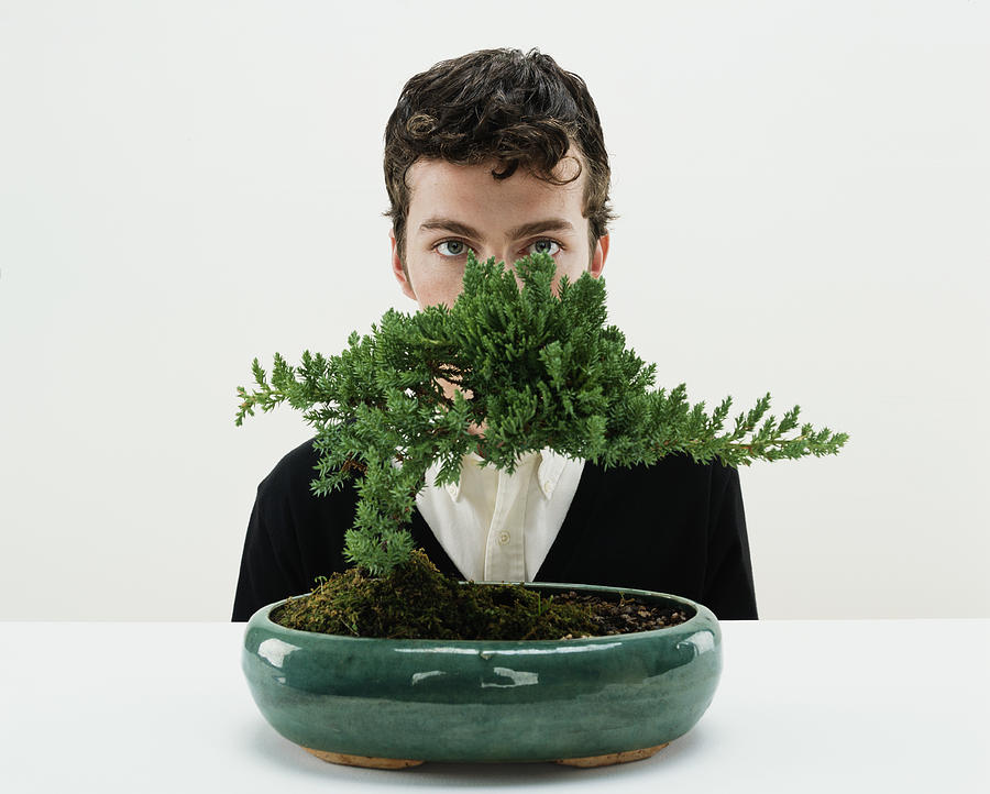 Young man behind bonsai tree, portrait Photograph by Digital Vision