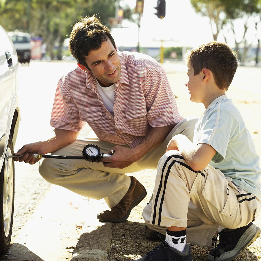 Young man checking the air pressure of car tire with his son Photograph by Stockbyte