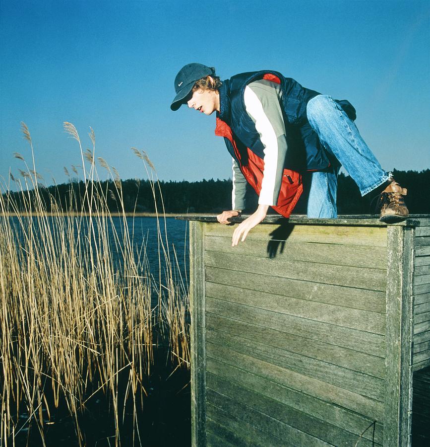 Young man climbing above wooden barrier by a lake Photograph by Ausloeser/Fuse