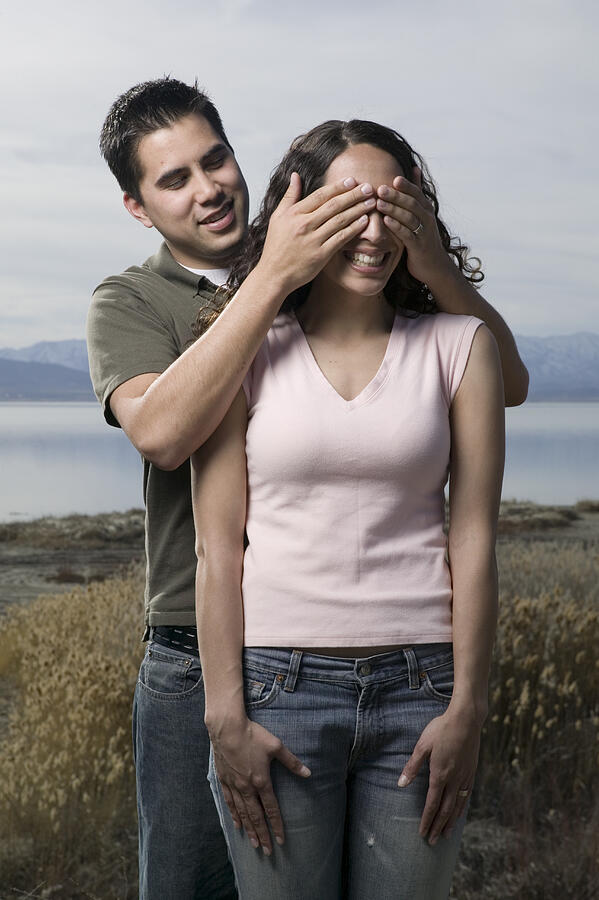 Young man covering young woman eyes, outdoors Photograph by Photodisc