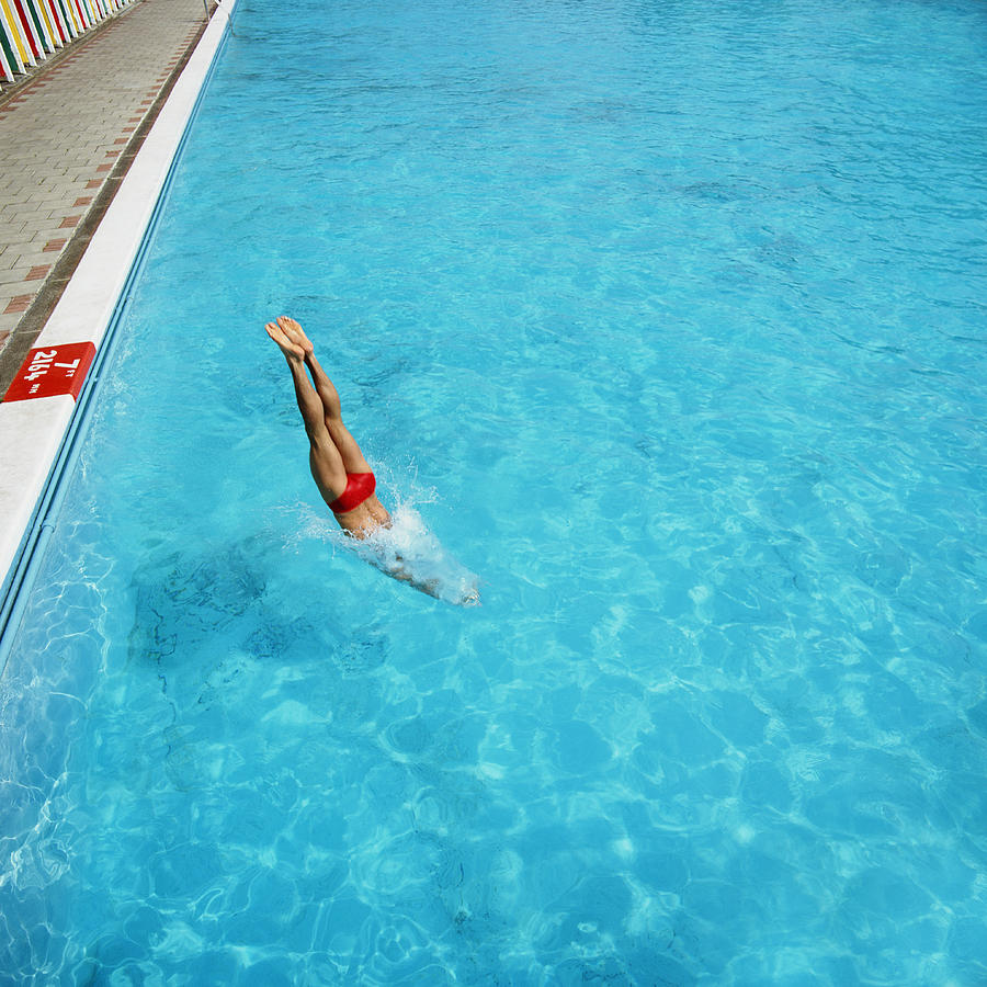 Young man diving head first into swimming pool Photograph by Peter Dazeley