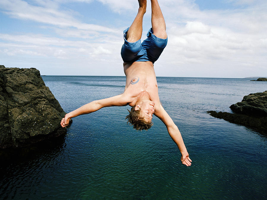 Young man doing somersault into water below Photograph by Mike Powell