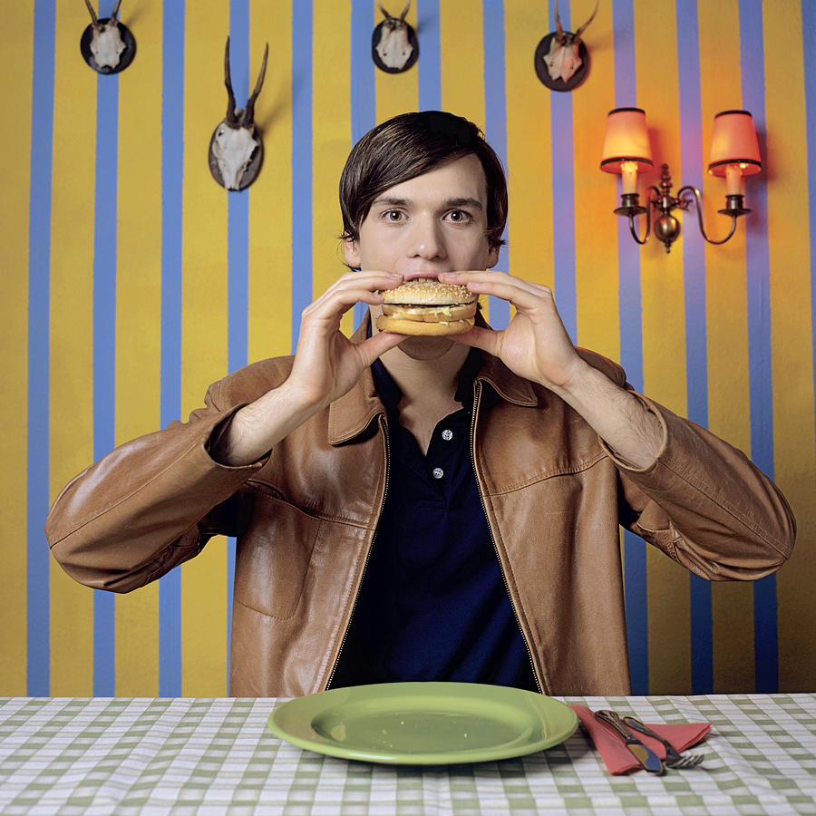 Young man eating burger, portrait Photograph by Jacob Lindner