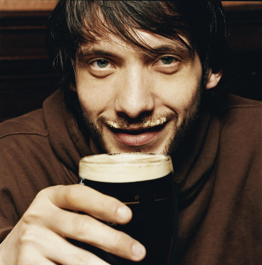 Young Man Enjoying a Drink of Stout in a Pub Photograph by Digital Vision.