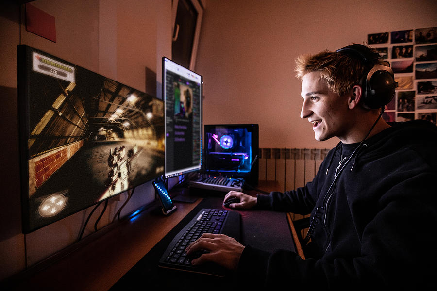 Young Man Enjoying Playing Online Multiplayer Games with his Friends while Locked in Quarantine - stock photo Photograph by CasarsaGuru