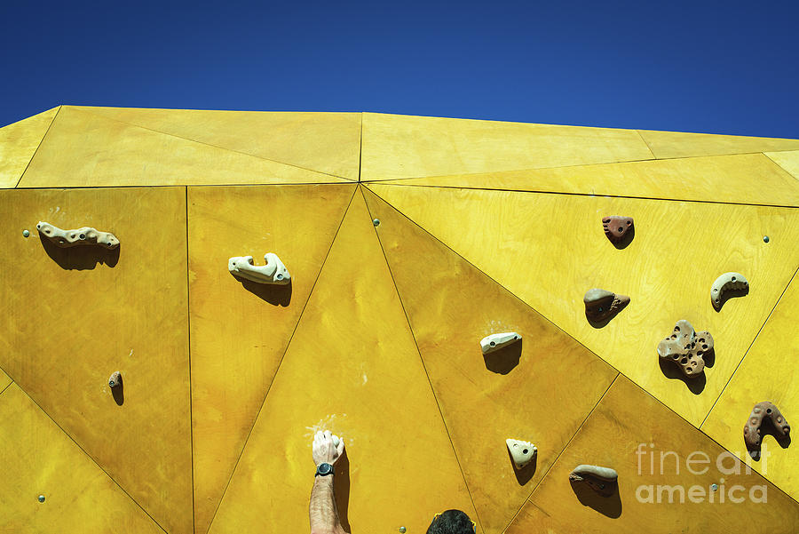 Young man grabs to try climbing on an outdoor climbing wall in a Photograph by Joaquin Corbalan