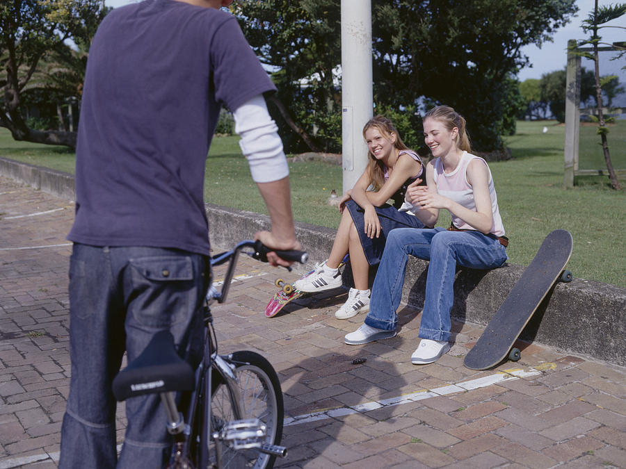 Young man holding bike talking to young women sitting on curb Photograph by Dex Image