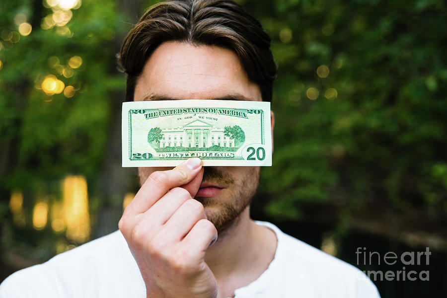 Young man holds a dollar bill in front of his face, corruption c Photograph by Joaquin Corbalan
