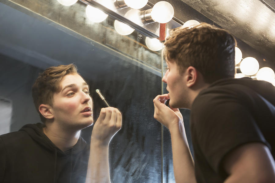 Young man in dressing room applying make-up Photograph by Kali9