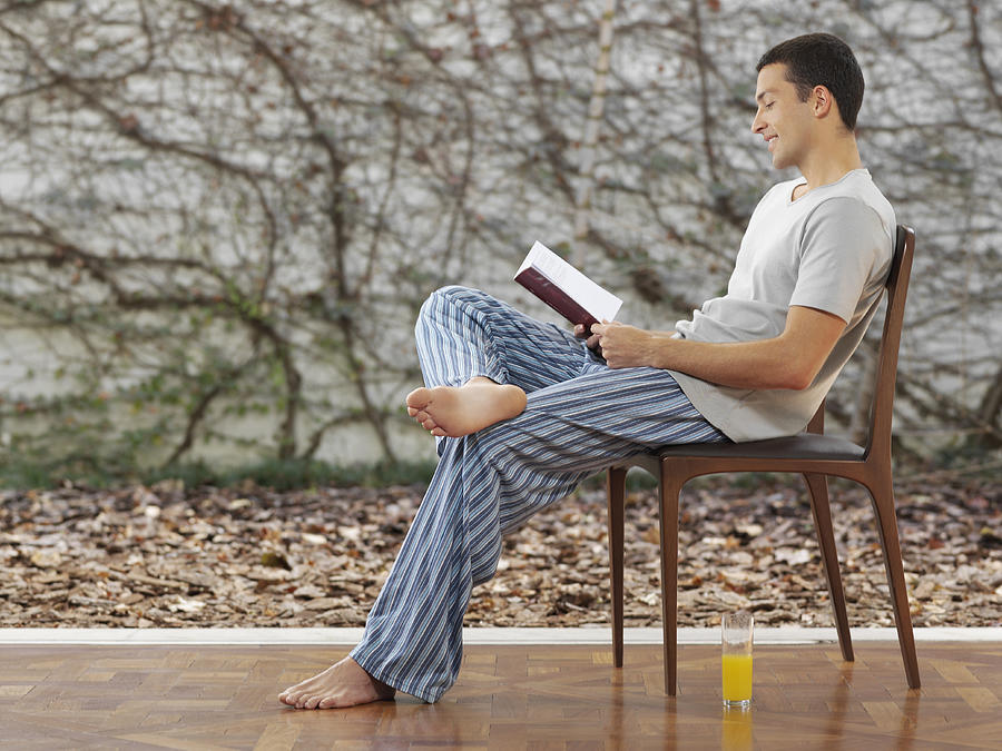 Young man in pajamas reading book, side view Photograph by Commercial Eye