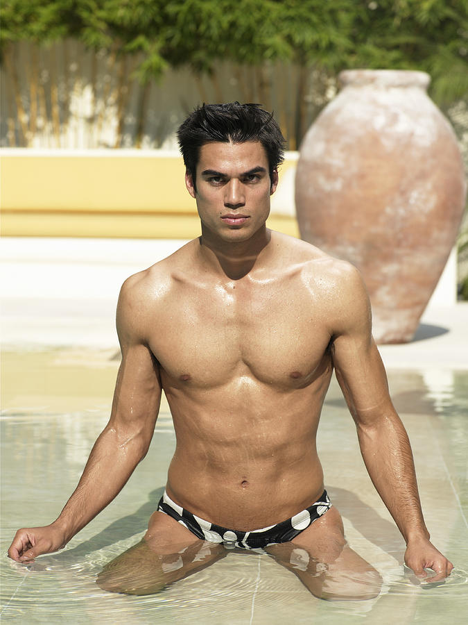 Young man in racing briefs kneeling in swimming pool, portrait Photograph by Ryan McVay