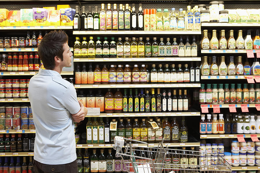 Young man in supermarket looking at bottles on shelves, close-up Photograph by Noel Hendrickson