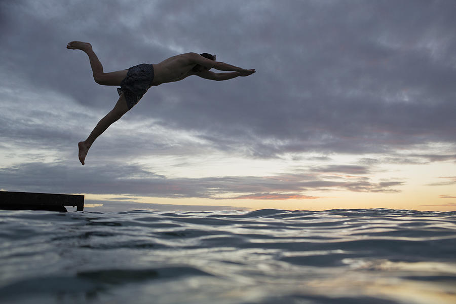Young man jumping into water at sunset Photograph by Felix Wirth