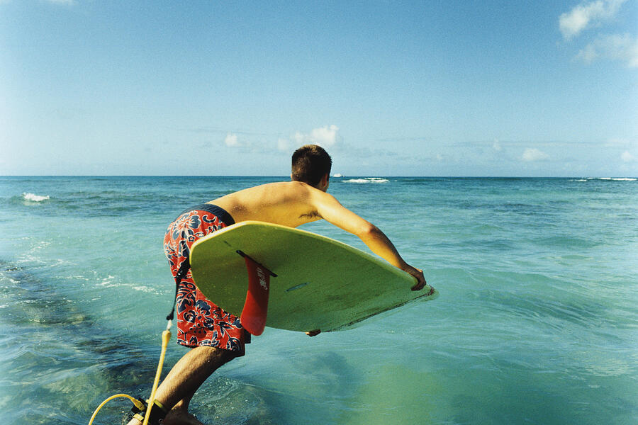 Young man jumping off with surfboard, rear view Photograph by Dex Image