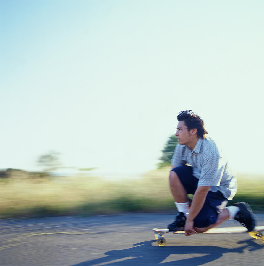 Young man kneeling down on longboard, side view (blurred motion) Photograph by Chad Baker/Jason Reed/Ryan McVay
