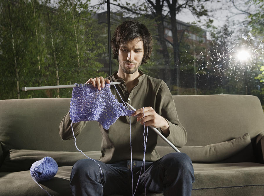 Young man knitting on sofa in livingroom Photograph by Betsie Van der Meer