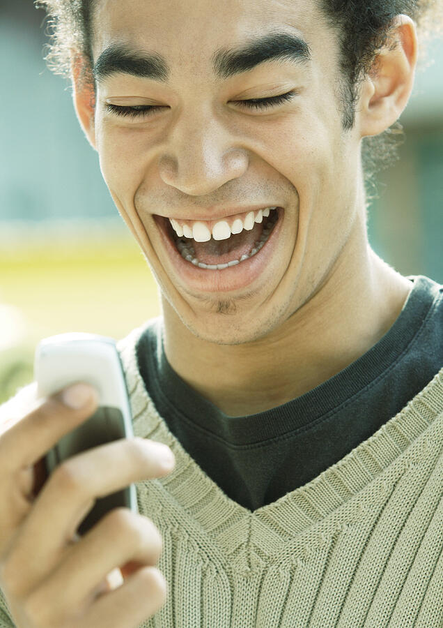 Young man laughing and looking at cell phone, close-up Photograph by Odilon Dimier