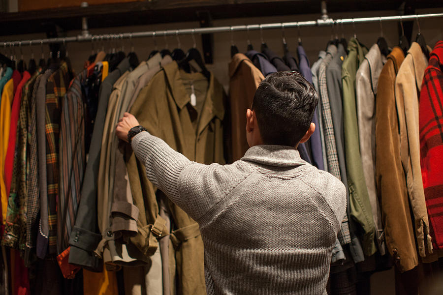Young man looking through clothes rail in vintage shop Photograph by Raphye Alexius