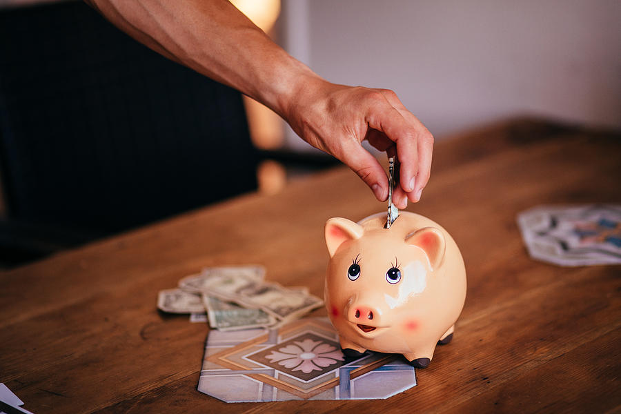 Young man saving money in a piggy bank at home Photograph by Wundervisuals