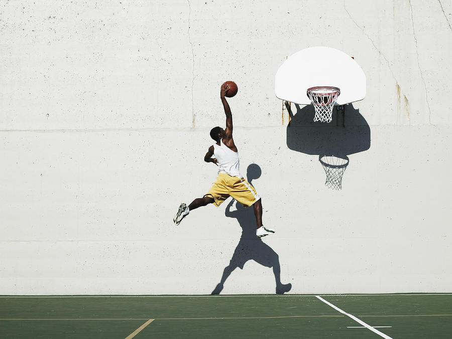 Young man shooting at basketball hoop on outdoor court, side view Photograph by Thomas Barwick