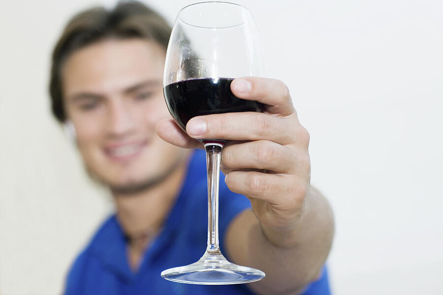 Young man showing a wine glass and smiling Photograph by Glowimages