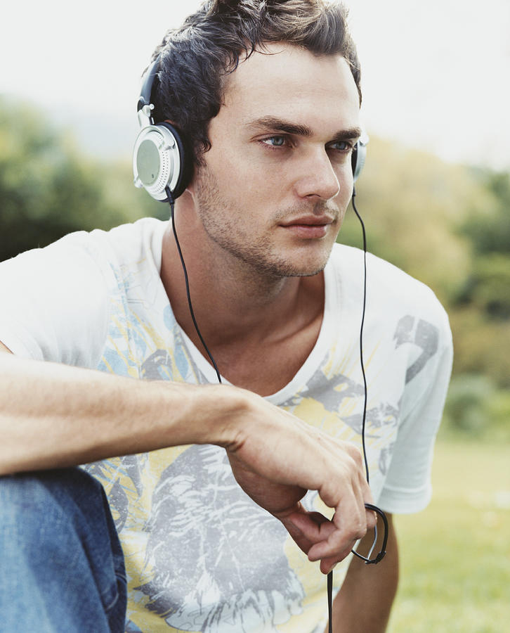 Young Man Sitting on Grass Listening to Music on His Headphones Photograph by Digital Vision.