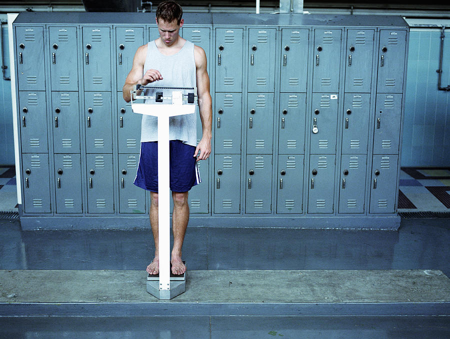 Young man stading on scale in locker room Photograph by Mike Powell