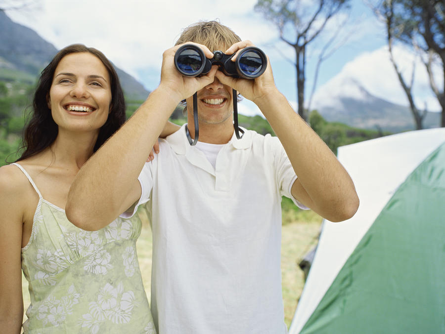 Young man standing with a Young woman and looking through binoculars Photograph by Stockbyte
