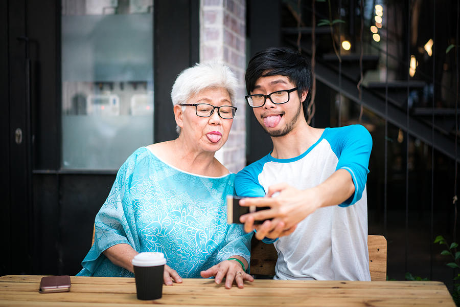 Young man taking a funny selfie with his grandmother Photograph by Yongyuan